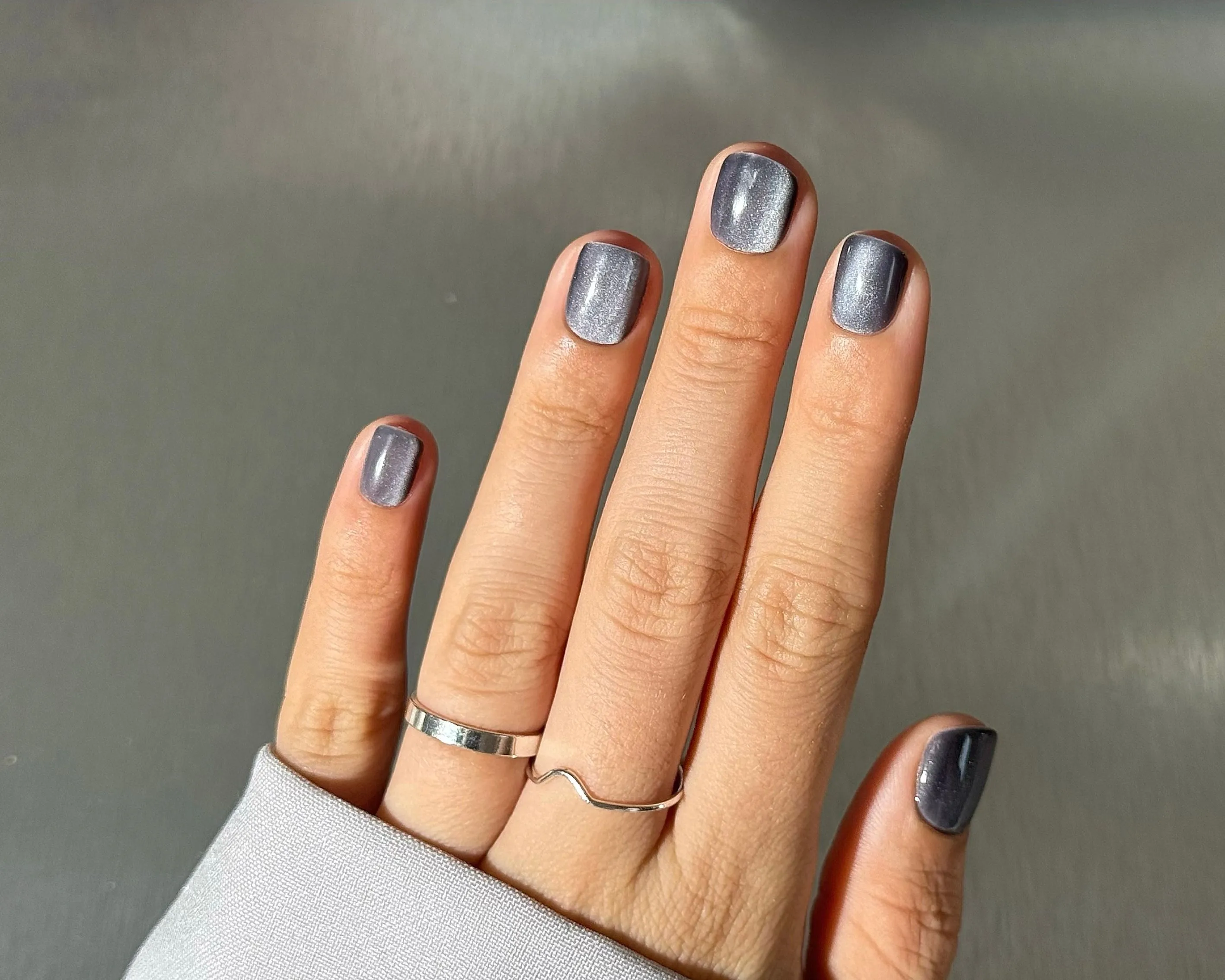 Hand displaying glossy grey cat-eye nail polish with a minimalist silver ring.