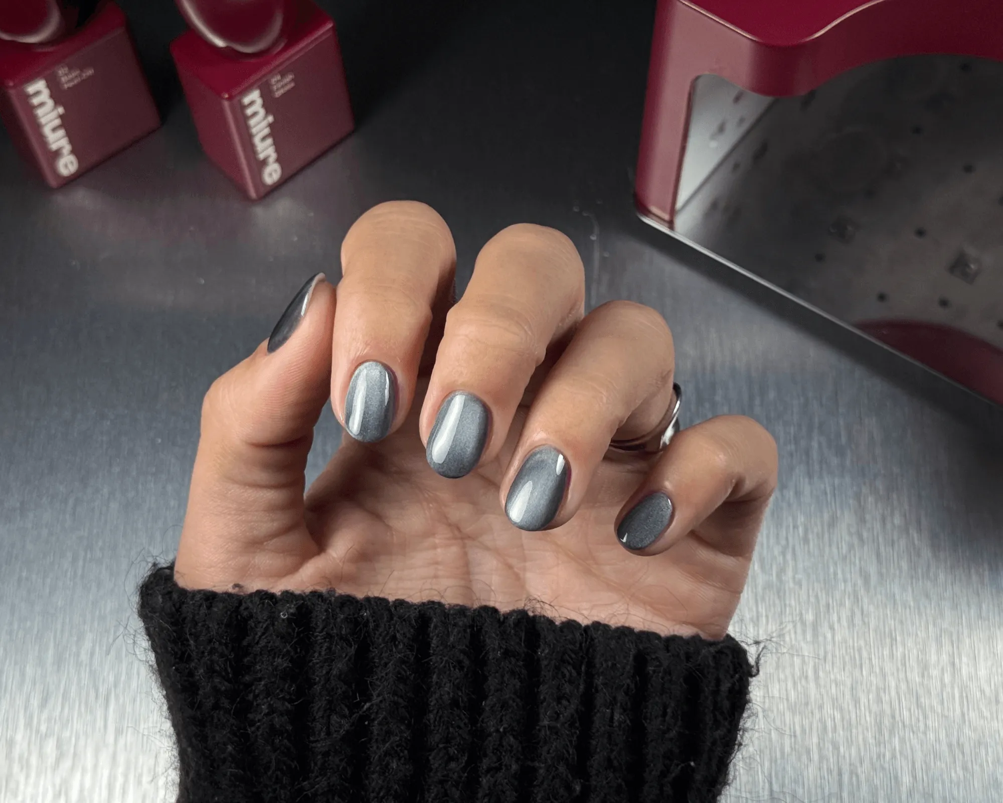 Hand with shiny grey metallic manicure, featuring a cat-eye effect on the nails.